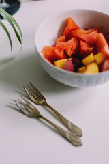 bowl of sliced fruits and two forks on a table