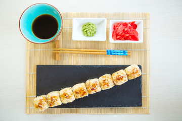 Set of hot lava maki japanese sushi rolls with fried scallop on a box at decorated with flowers, bamboo and cloth wooden table background. Healthy and tasty food.