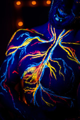 Obraz premium UV patterns body art of the circulatory system on a man's body. On the torso of a muscular athlete, veins and arteries are drawn with fluorescent dyes. Bodybuilder standing by the mirror with lamps.