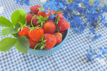 strawberries in a blue bowl on a checkered tablecloth and a bouquet of blue flowers close-up. background with fresh strawberries and a bouquet of wild flowers.