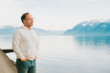 Portrait of handsome man admiring beautiful lake with mountains, wearing white sweatshirt