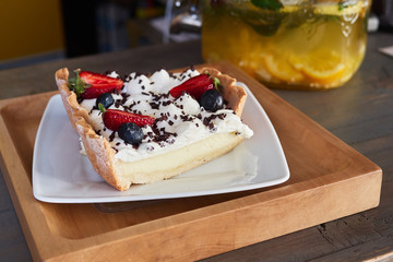 Craft fresh baked delicious strawberry and blueberry cheesecake stacked with cream mousse served on white ceramic plate in cozy city cafe photographed with natural light in warm vintage film colors.