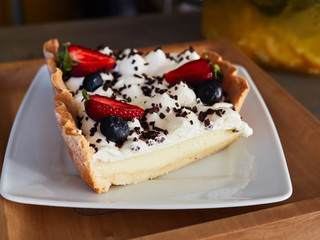 Craft fresh baked delicious strawberry and blueberry cheesecake stacked with cream mousse served on white ceramic plate in cozy city cafe photographed with natural light in warm vintage film colors.