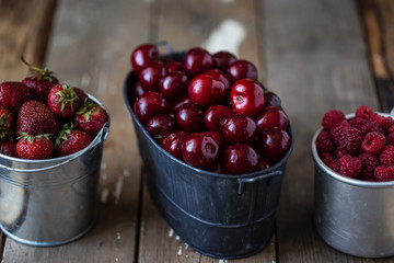 harvest of summer berries. Strawberries, cherries, raspberries in pails on a wooden table. Country style