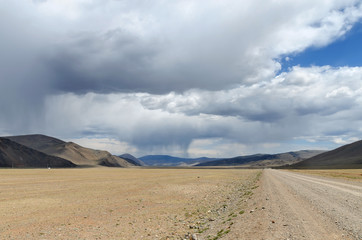Western Mongolia steppe landscape. Dirt road and rain ahead. Outskirts Tsagaannuur, Bayan-Ulgii Province, Mongolia.