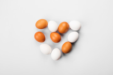 Group of raw eggs white and brown in shape of heart. On gray background. Top view