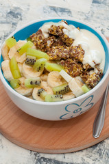 Greek yogurt and granola kiwi, banana in bowl with a spoon on a gray concrete background, view from the top. Fitness diet for weight loss, proper nutrition and a healthy lifestyle