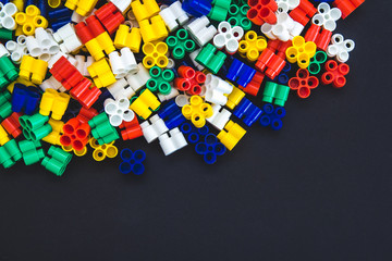 Multicolored plastic blocks on a black background with a place for text. Parts of the bright little spare parts for toys. Top view