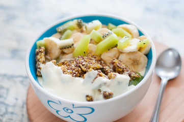 Greek yogurt, granola, kiwi and banana in bowl with a spoon on a gray concrete background, wooden tray, copy space. Fitness diet for weight loss, proper and tasty food