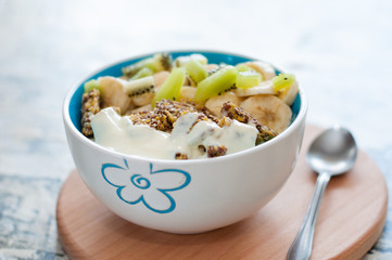 Greek yogurt, granola, kiwi and banana in bowl with a spoon on a gray concrete background, wooden tray, copy space. Fitness diet for weight loss, proper and tasty food