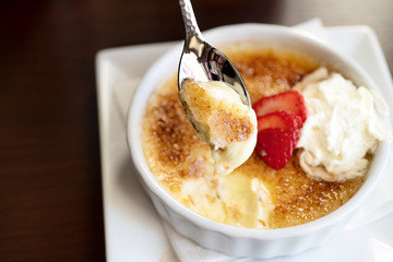 Creme brulee on a spoon garnished with whipped cream and a strawberry