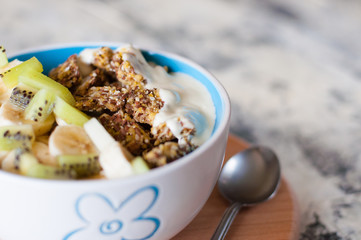 Greek yogurt, granola, kiwi and banana in a bowl on a gray concrete background, wooden tray, close-up. Fitness diet for weight loss, proper and tasty food