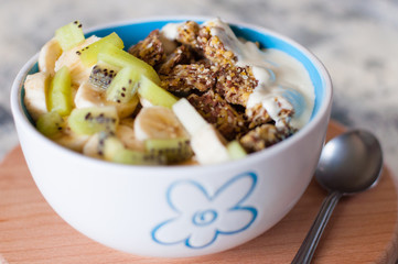 Greek yogurt, granola, kiwi and banana in a bowl on a gray concrete background, wooden tray, close-up. Fitness diet for weight loss, proper and tasty food