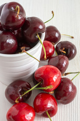 Close-up of cherries in white bowl on white wooden background in vertical