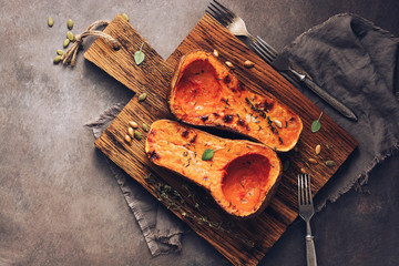 Delicious baked or butternut squash pumpkin with thyme on a cutting board, dark rustic background. Top view, flat lay. The concept of diet nutrition.