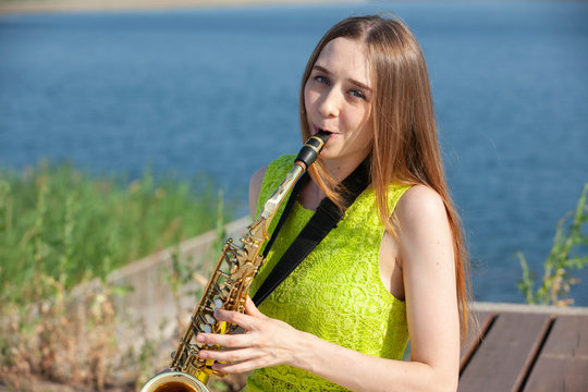Beautiful smiling girl with saxophone. Young beautiful saxophonist with saxophone - outdoor in nature.