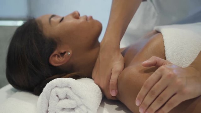 Profile side view of charming and beautiful woman lying on spa bed for traditional body massage therapy and beauty treatments. She spending free time inside bright and light salon interior