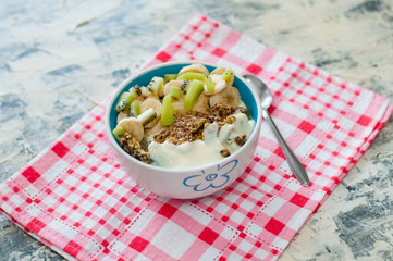Granola with Greek yogurt kiwi and banana in bowl with a spoon on a pink napkin, view from the top. Fitness diet for weight loss, proper and tasty food