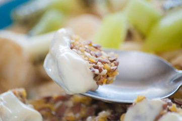 Piece of dessert on spoon close-up. Granola with Greek yogurt, kiwi and banana in a bowl. View from the side. Fitness diet for weight loss, proper and tasty food