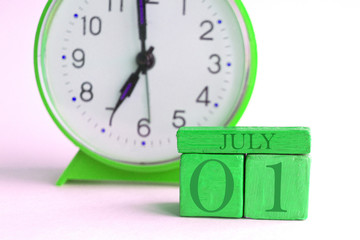 july 1st. Day 1 of month, handmade wood calendar and alarm clock on light green color. summer month, day of the year concept