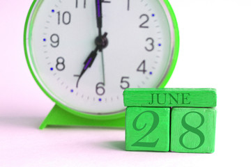 june 28th. Day 28 of month, handmade wood calendar and alarm clock on light green color. summer month, day of the year concept