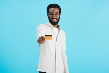 cheerful african american man showing credit card isolated on blue