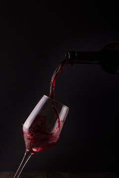 compa con vino tinto cayendo de la botella con fondo oscuro