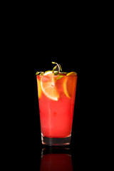 Red lemonade with some vegetable leaves and a few slices of lemon on the black isolated background
