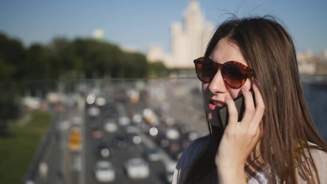 Young pretty woman talking on the phone on a city bridge. Traffic on background.