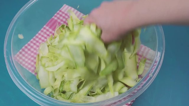 Grated cucumber or green pumpkin on blue background. Woman hands shaking vegetables. Vegetarian food concept