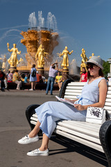 Obraz premium Happy young and stylish woman with hat and book sitting on the bench in the park.