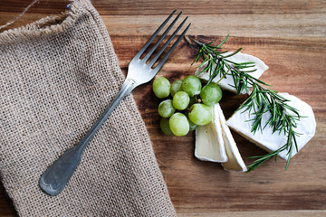 Käseplatte, Käse und Rosmarin mit Besteck auf einer Holzplatte
