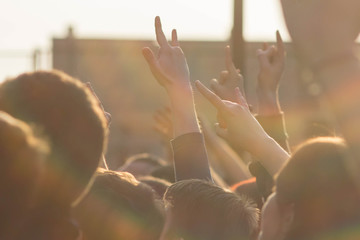 Crowd of fans raising their hands up and showing rocker symbols and palms to performing artists on stage. Sign of the horns on open air rock concert.