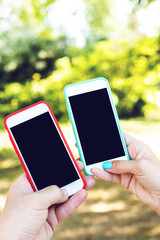 Two smartphones in woman and man hands on a nature background. Black screens.