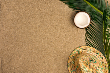 Fototapeta na wymiar Beach theme on the sand background. Palm leaves, coconut, hat on the sand. Top view.