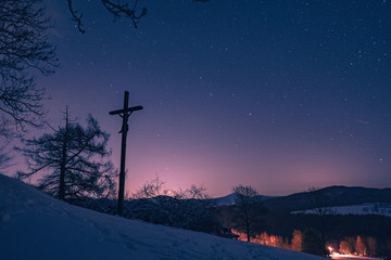 Winterlandschaft bei Nacht mit Sternenhimmel und Jesuskreuz im Vordergrund