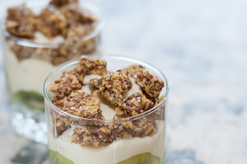 Granola, kiwi, banana and Greek yogurt in two glass cups on gray concrete, copy space. Fitness, figure, body and healthy food