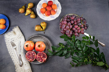 Still life. Fruits and green leaves on the table. Pomegranates, apricots, black grapes, pears and apples.