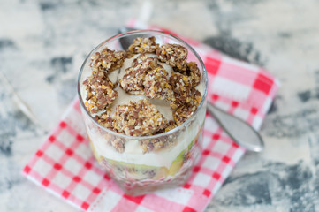 Granola, Greek yogurt, kiwi and banana in glass beaker on a checkered pink napkin gray concrete, with a spoon to copy space, view from the top. Fitness, figure, body and healthy food