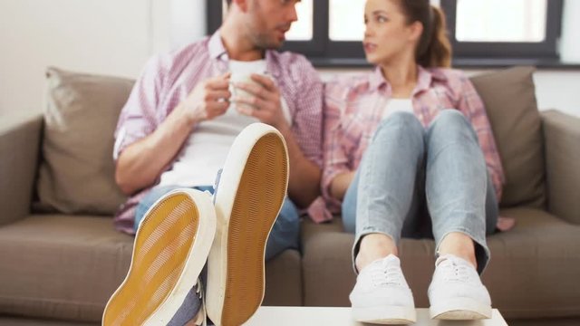 people and leisure concept - feet of couple drinking coffee at home on table