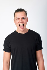 Obraz premium Funny cheerful attractive stylish man wearing a black cotton T-shirt have fun, showing tongue, posing in studio. Studio shot on a white background.
