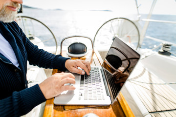 Digitaler Nomade mit Laptop arbeitet auf einem Segelboot - Nahaufnahme Hände über der Tastatur