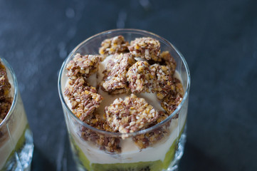 Greek yogurt, granola, banana and kiwi. Dessert in glass beaker on a dark background, close-up macro. Concept body and healthy food