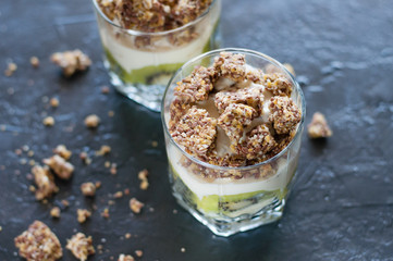 Greek yogurt, granola, banana and kiwi. Desserts in glass cups on dark background, side view from the top. Concept body and healthy food
