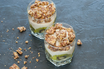 Greek yogurt, granola, banana and kiwi. Desserts in glass cups on dark background, side view from the top. Concept body and healthy food