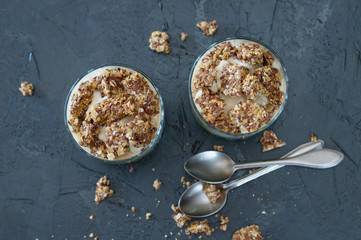Greek yogurt, granola, banana and kiwi. Desserts in glass with spoons on a dark background, flat lay. Concept body and healthy food