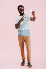 Fototapeta premium african american man in sunglasses with victory sign taking selfie on smartphone, isolated on pink