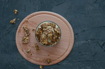 Granola, banana, kiwi and greek yogurt. Dessert in a glass cup on a wooden round board, dark background, flat Lay. Concept body and healthy food