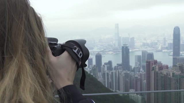 Traveling woman photographing Hong Kong city panorama while travel vacation. Tourist woman taking photo city panorama from Peak Victoria in Hong Kong city, China. Tourism and travel.