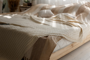 Closeup of comfort double bed with beige pillows and blanket, sun beams and shadows in cozy bedroom.